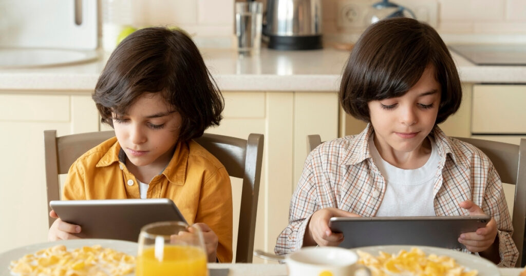 Criança utiliza celular durante a refeição enquanto faz uma refeição à mesa