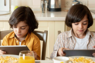 Criança utiliza celular durante a refeição enquanto faz uma refeição à mesa